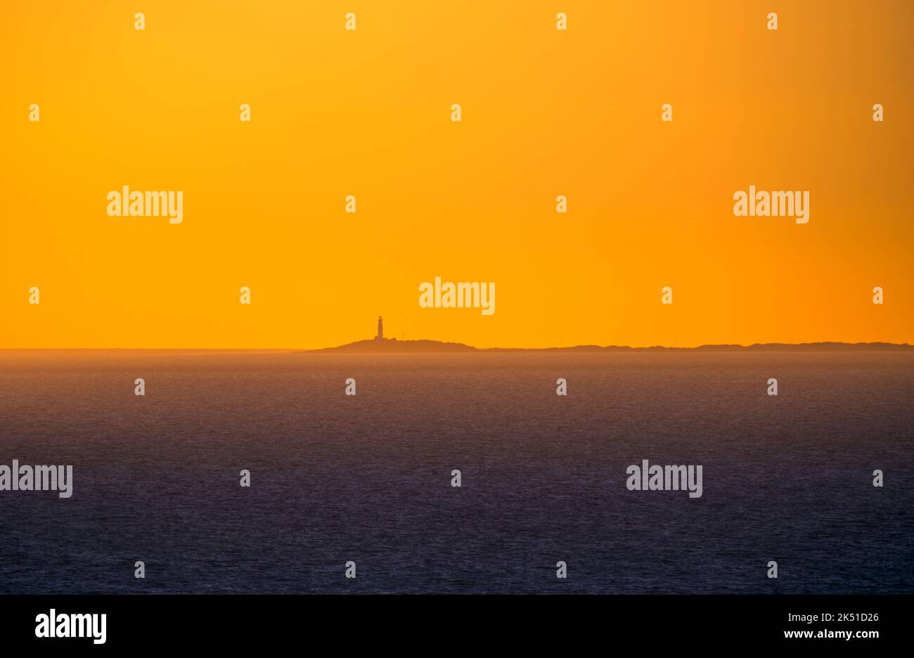 Maestoso paesaggio di faro distante su un piccolo isolotto in acqua di mare blu scuro con il cielo vivido arancio tramonto sopra Foto Stock