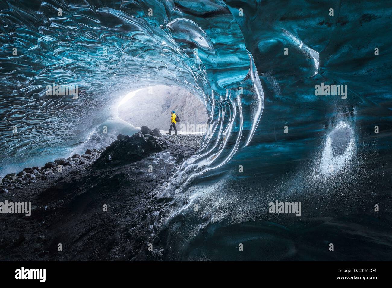 Turista in outerwear in piedi vicino a buche irregolari in superficie di ghiaccio, mentre esplorare la grotta nel ghiacciaio Vatnajokull il giorno d'inverno in Islanda Foto Stock