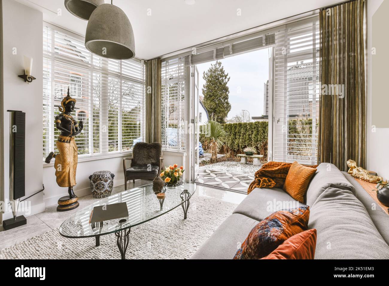 Interno di spazioso soggiorno con decor asiatico e divano davanti alle finestre a lunghezza intera che si affacciano sulla terrazza Foto Stock