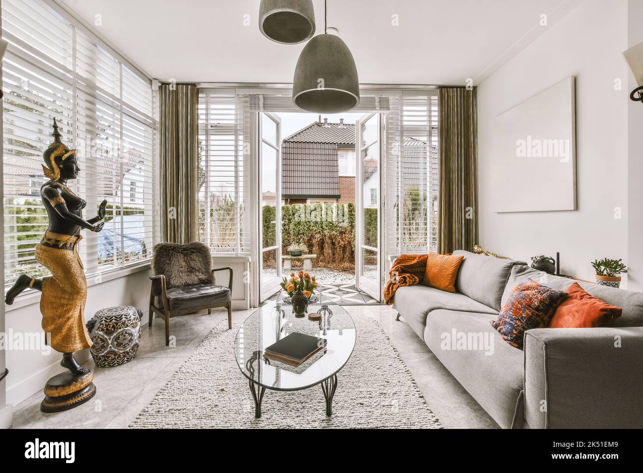 Interno di spazioso soggiorno con decor asiatico e divano davanti alle finestre a tutta lunghezza che si affacciano sul cortile Foto Stock