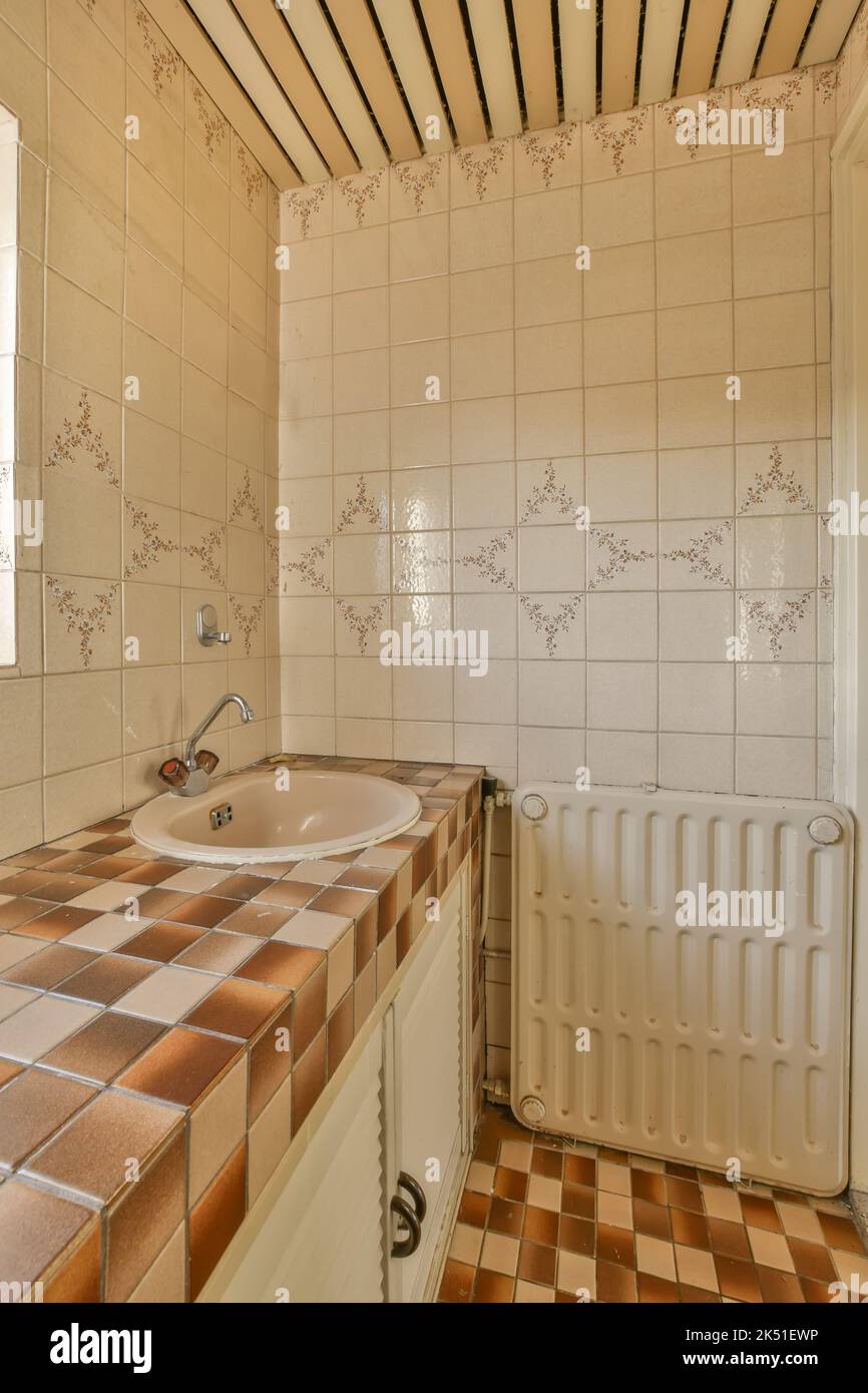Lavabo in ceramica con rubinetto cromato vicino al radiatore in antico bagno d'epoca con pareti in mosaico Foto Stock