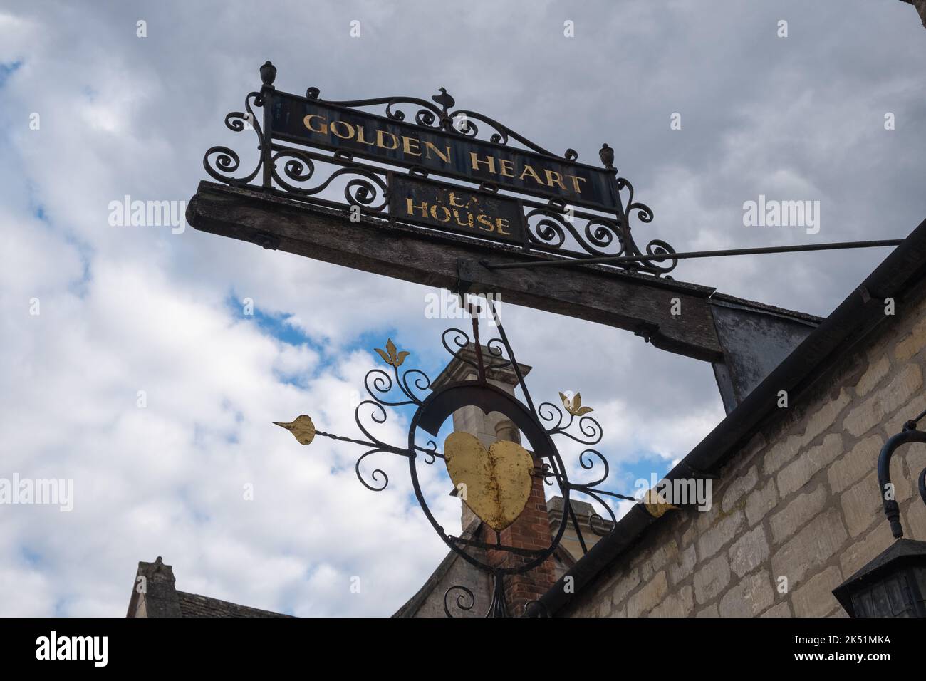 Segno ornato appeso fuori di una casa Cotswold, casa cuore dorato, con un cuore con una freccia attraverso di esso Foto Stock