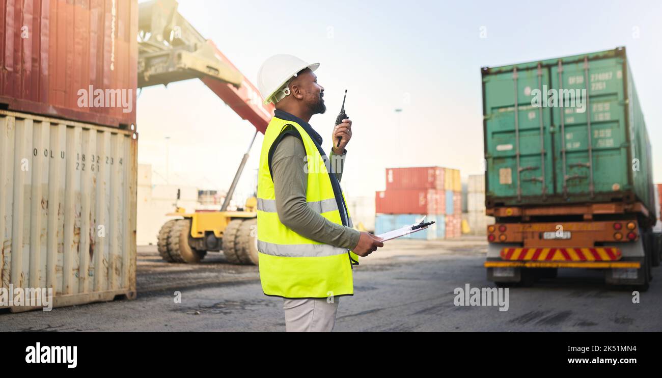 Uomo nero che lavora su stock, logistica e consegna del carico nel settore dei trasporti e della catena di fornitura presso il porto marittimo. Dipendente con radio Foto Stock