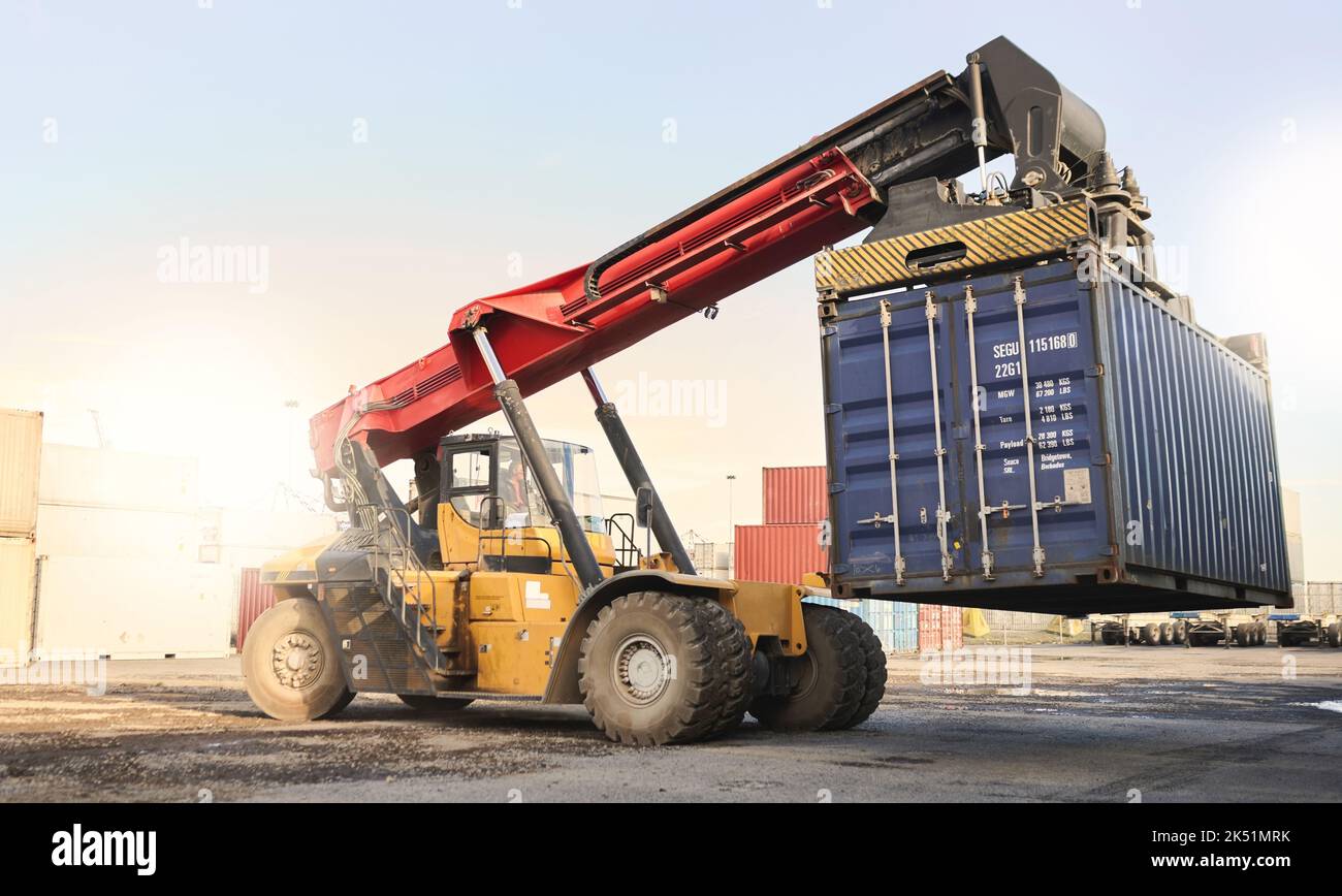 Trasporto, logistica e supply chain con stoccaggio di container e un veicolo a gru su un molo commerciale. Spedizione, carico e trasporto in un cortile vuoto Foto Stock
