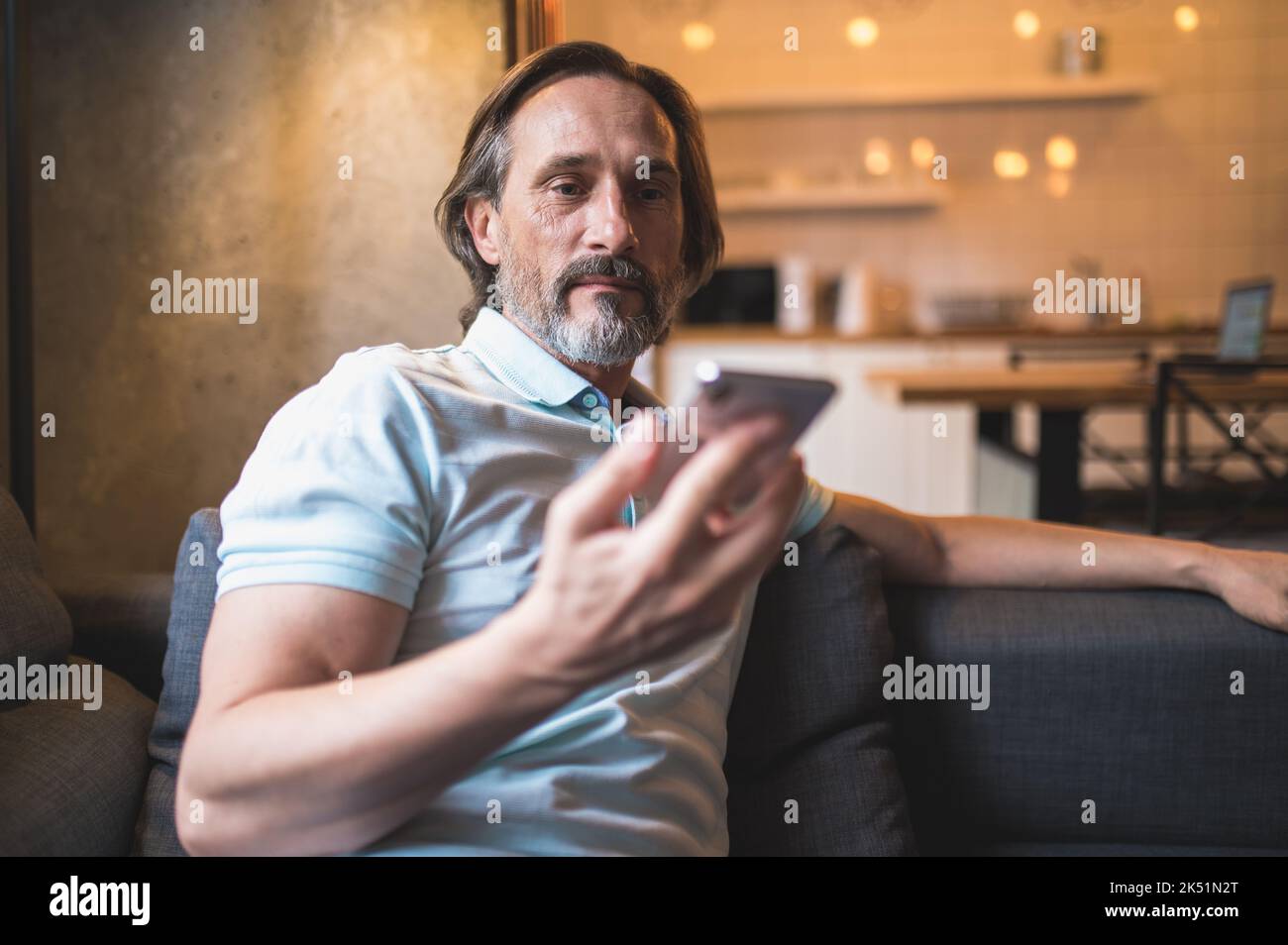 Uomo bearato seduto in poltrona acon uno smartphone in mano Foto Stock