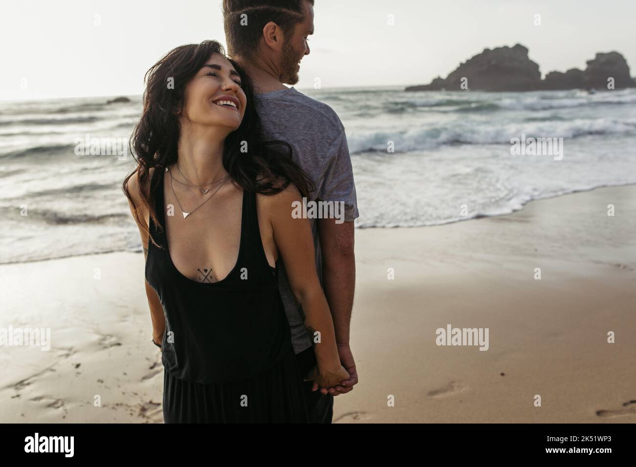 donna felice e uomo bearded che si levano in piedi indietro e che tiene le mani vicino oceano, immagine di riserva Foto Stock