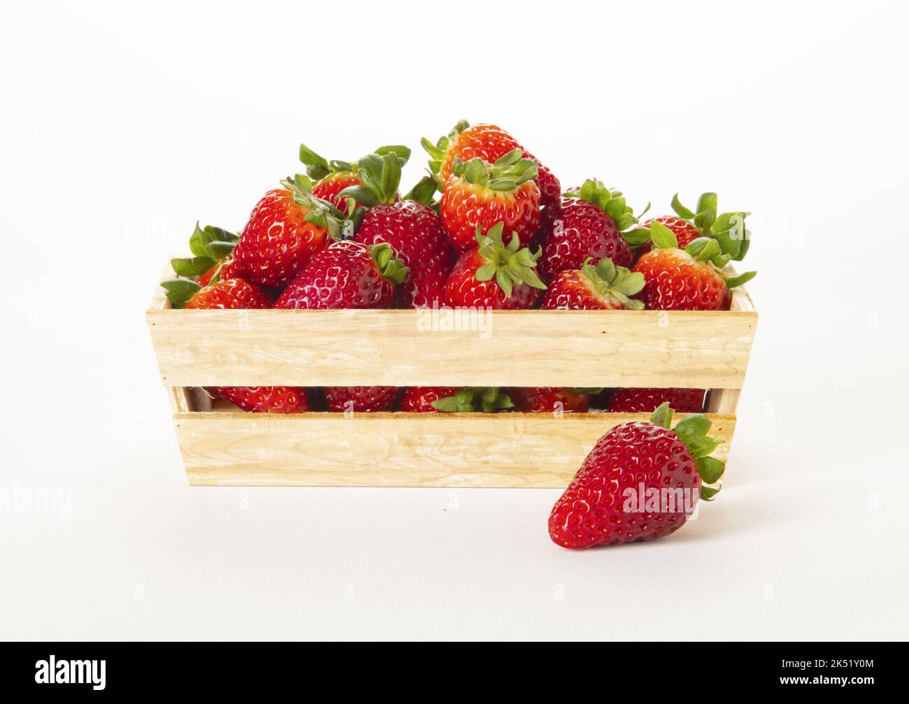 Cestino di legno pieno di fragole con uno fuori sulla superficie. Su sfondo bianco. Foto Stock