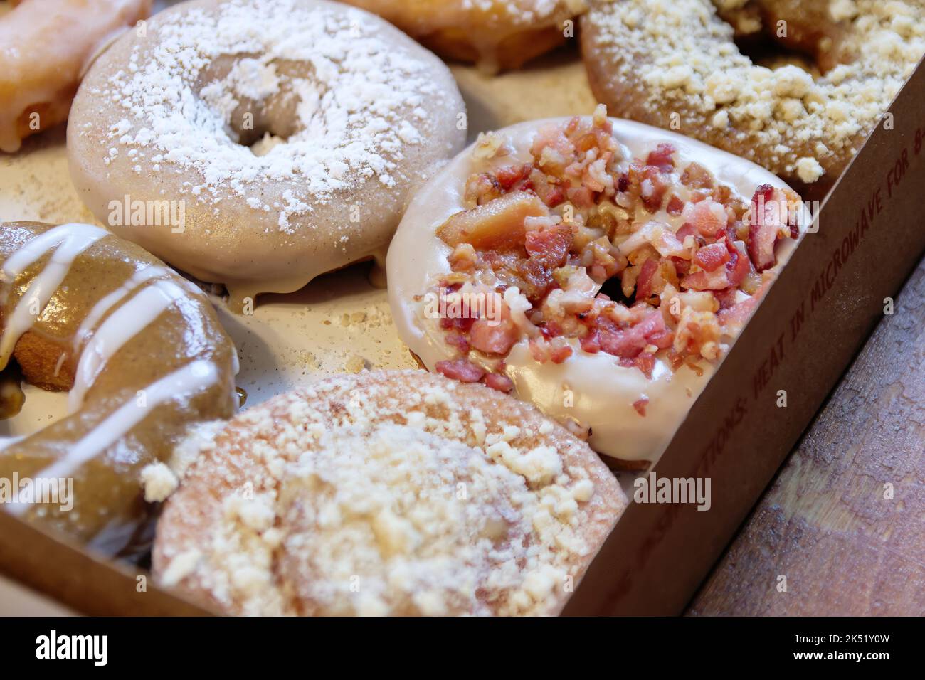 Immagine di ciambelle assortite in una scatola con ciambelle al cioccolato, in polvere e cosparse di pancetta. Foto Stock