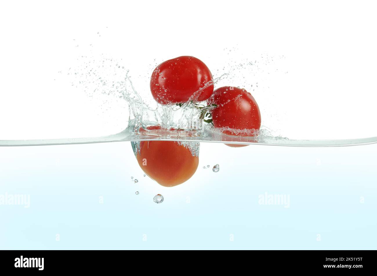 Tre pomodori che spruzzano in acqua. Vista laterale su sfondo bianco. Foto Stock