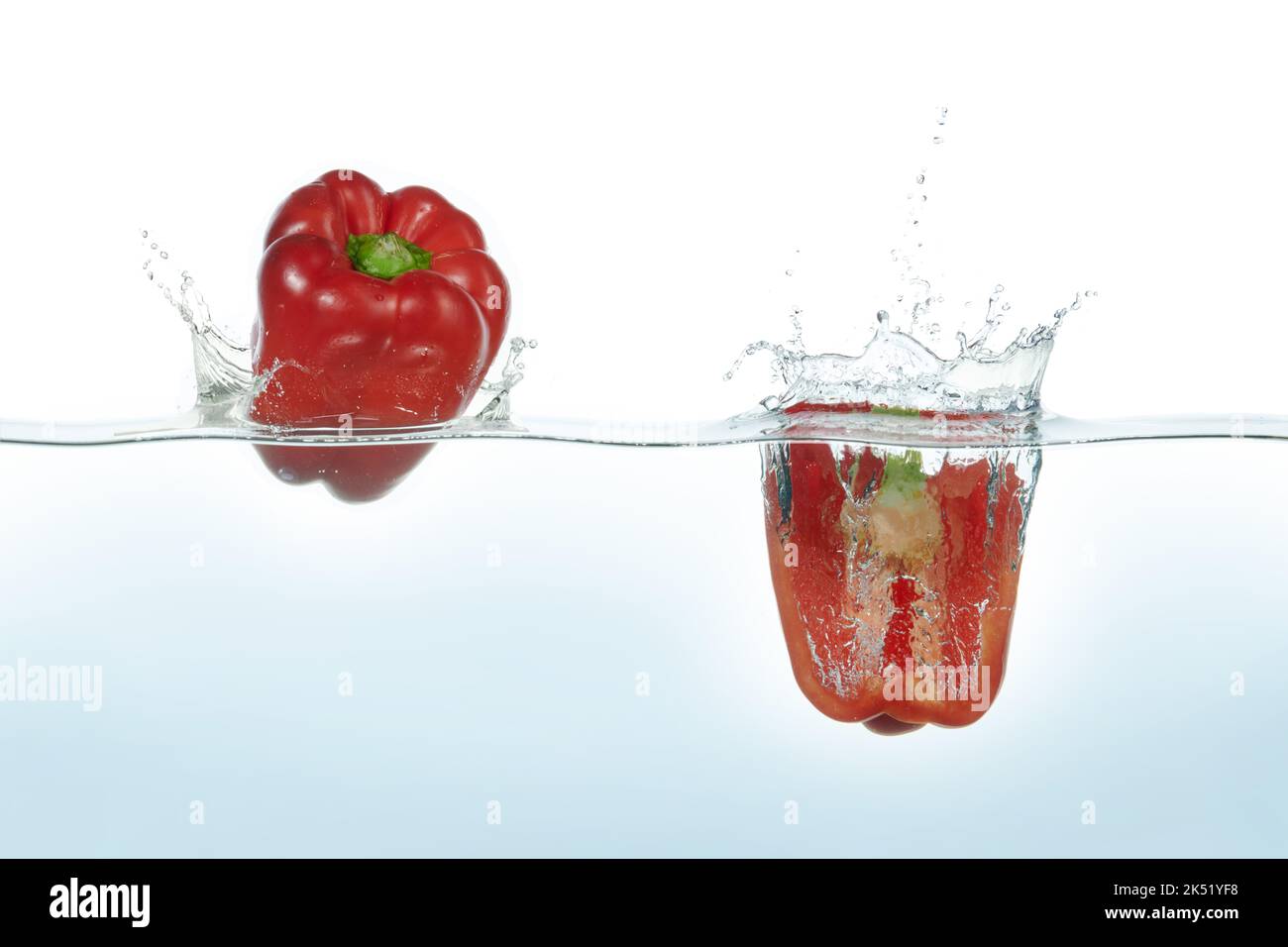 Due peperoni rossi che spruzzano in acqua. Vista laterale su sfondo bianco. Foto Stock