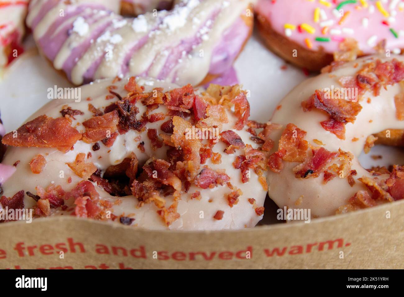 Immagine di ciambelle assortite in una scatola con la guarnizione di bacon, glassato rosa, e spruzzare ciambelle. Foto Stock