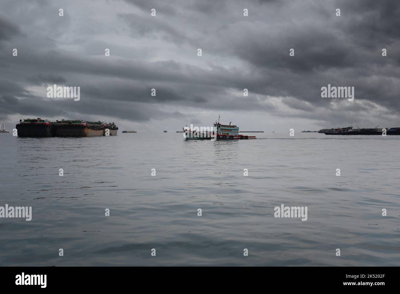 Barche da rimorchiatore e navi da carico ormeggiate nella baia di Koh Sichang, provincia di Chonburi in Thailandia, il cielo coperto e la pioggia in arrivo. Foto Stock