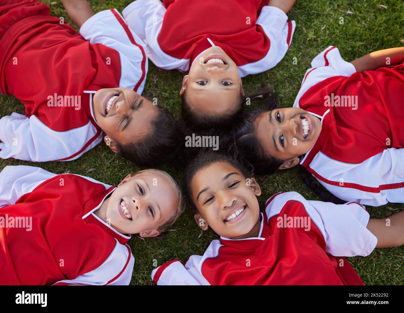 Felice calcio bambini rilassarsi sul campo sport ritratto per la collaborazione di gruppo, il lavoro di squadra e la motivazione. Calcio ragazza bambini faccia sdraiato a terra Foto Stock