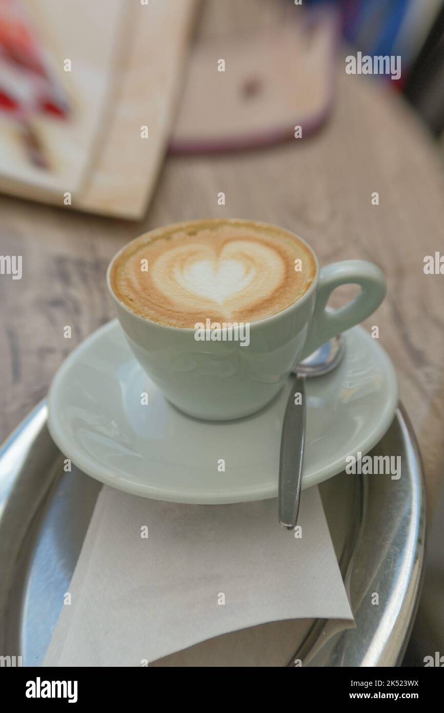 Una tazza di cappuccino con un cuore di schiuma di latte sul vassoio d'argento Foto Stock