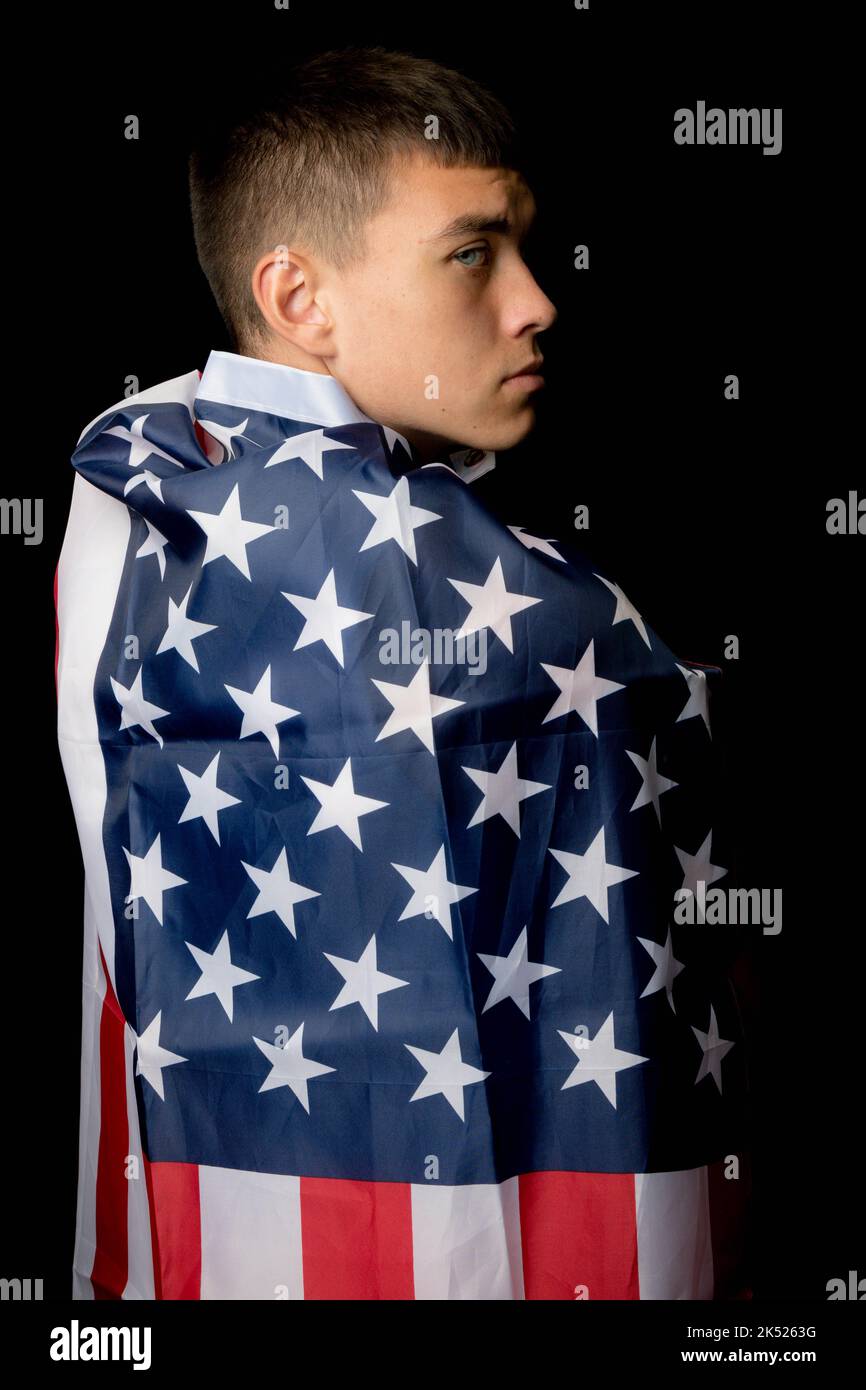 Ritratto di un ragazzino di diciannove anni su sfondo nero con una bandiera americana da dietro Foto Stock