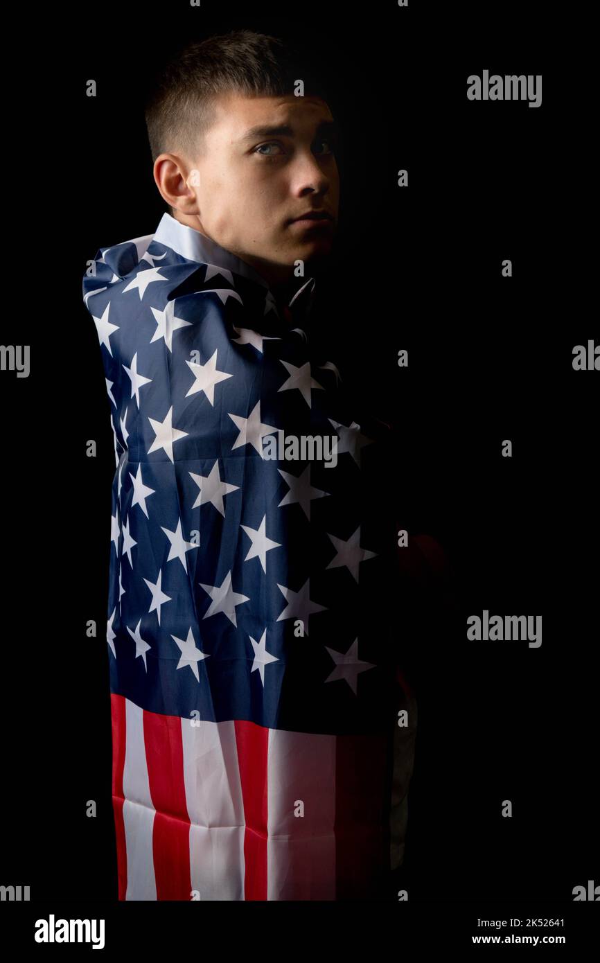 Ritratto di un ragazzino di diciannove anni su sfondo nero con una bandiera americana da dietro Foto Stock
