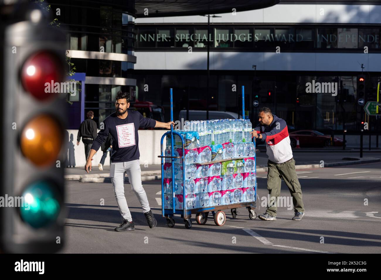 I lavoratori manovrano un carrello che trasporta un gran numero di bottiglie di acqua minerale in una giornata calda a Londra, Inghilterra, Regno Unito Foto Stock