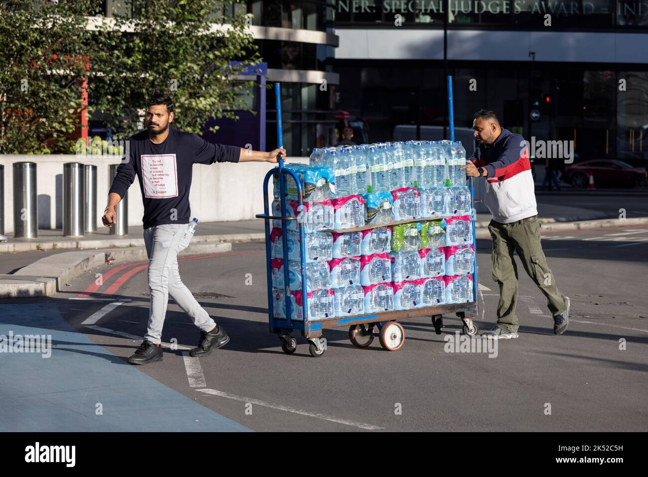 I lavoratori manovrano un carrello che trasporta un gran numero di bottiglie di acqua minerale in una giornata calda a Londra, Inghilterra, Regno Unito Foto Stock