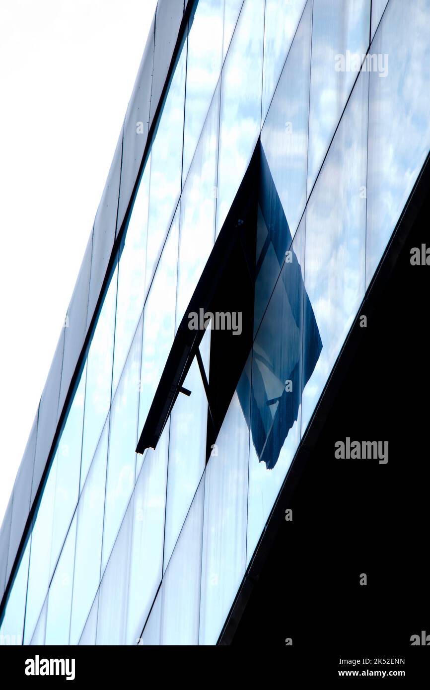 Astratto architettonico - una finestra aperta su un edificio con facciata in vetro con riflessi del cielo, vista ad angolo basso Foto Stock