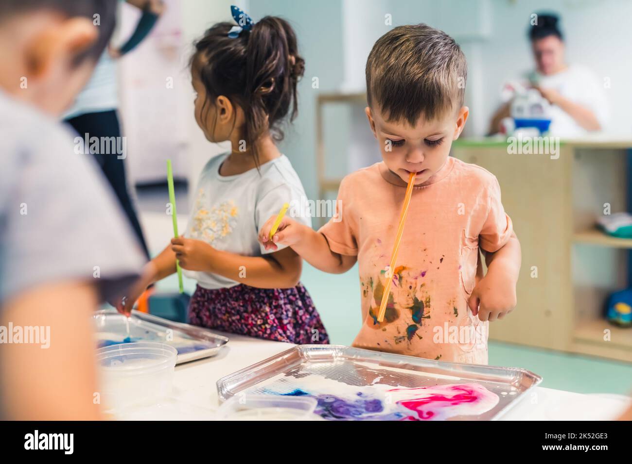 ragazzino che tiene un tubicino con la bocca per dipingere con vernici ad acqua, idea dei bambini da scuola materna a tiro medio. Foto di alta qualità Foto Stock