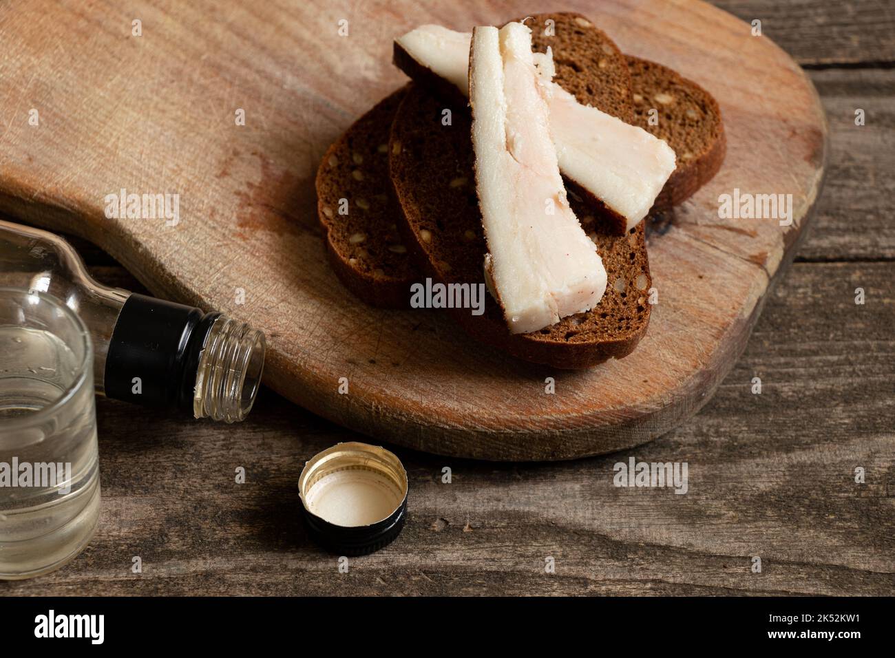 un pezzo di pane con pancetta un bicchiere di vodka sul tavolo, bevande alcoliche e uno spuntino, cattive abitudini, dipendenza da alcol, cibo e bevande Foto Stock