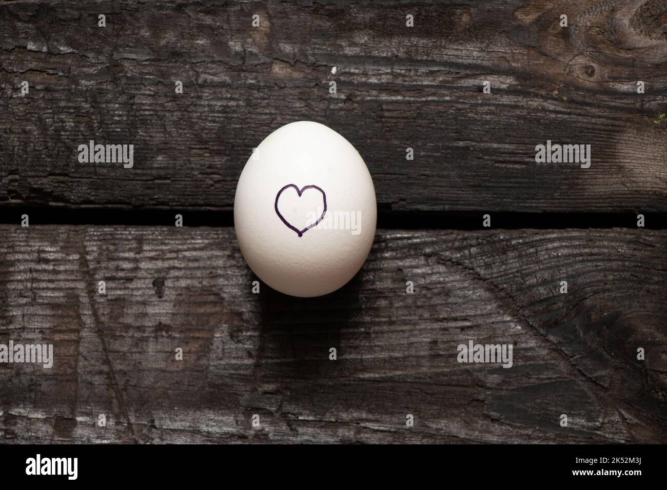 il cuore è disegnato su un uovo di pollo che si trova su un vecchio tavolo di legno, l'amore e le sensazioni Foto Stock