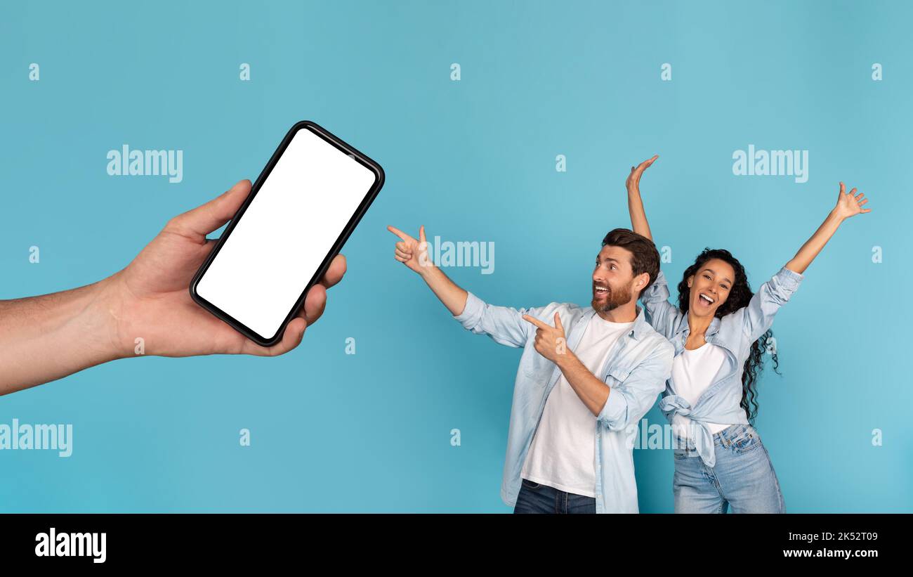 Felice eccitato giovane europeo e famiglia arabo punta le dita a smartphone con schermo vuoto in mano Foto Stock