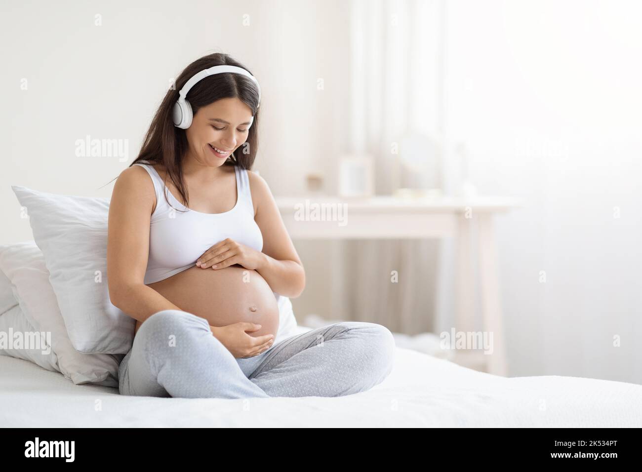 Felice giovane donna incinta sorridente che ascolta musica in cuffie Foto Stock