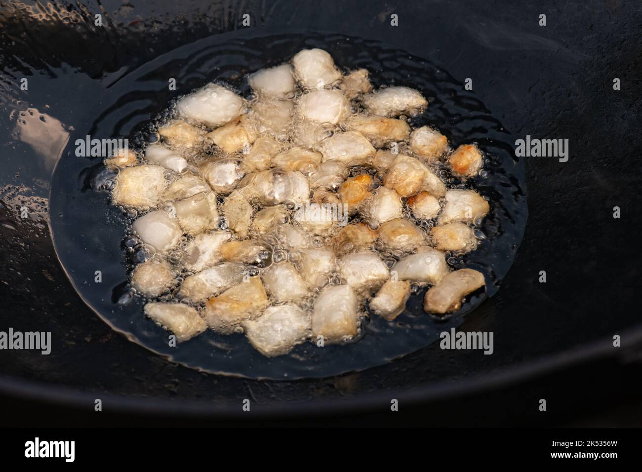 Grandi pezzi di coda grassa di agnello crudo fritti in olio con bolle in un primo piano di cottura nero cauldron Foto Stock