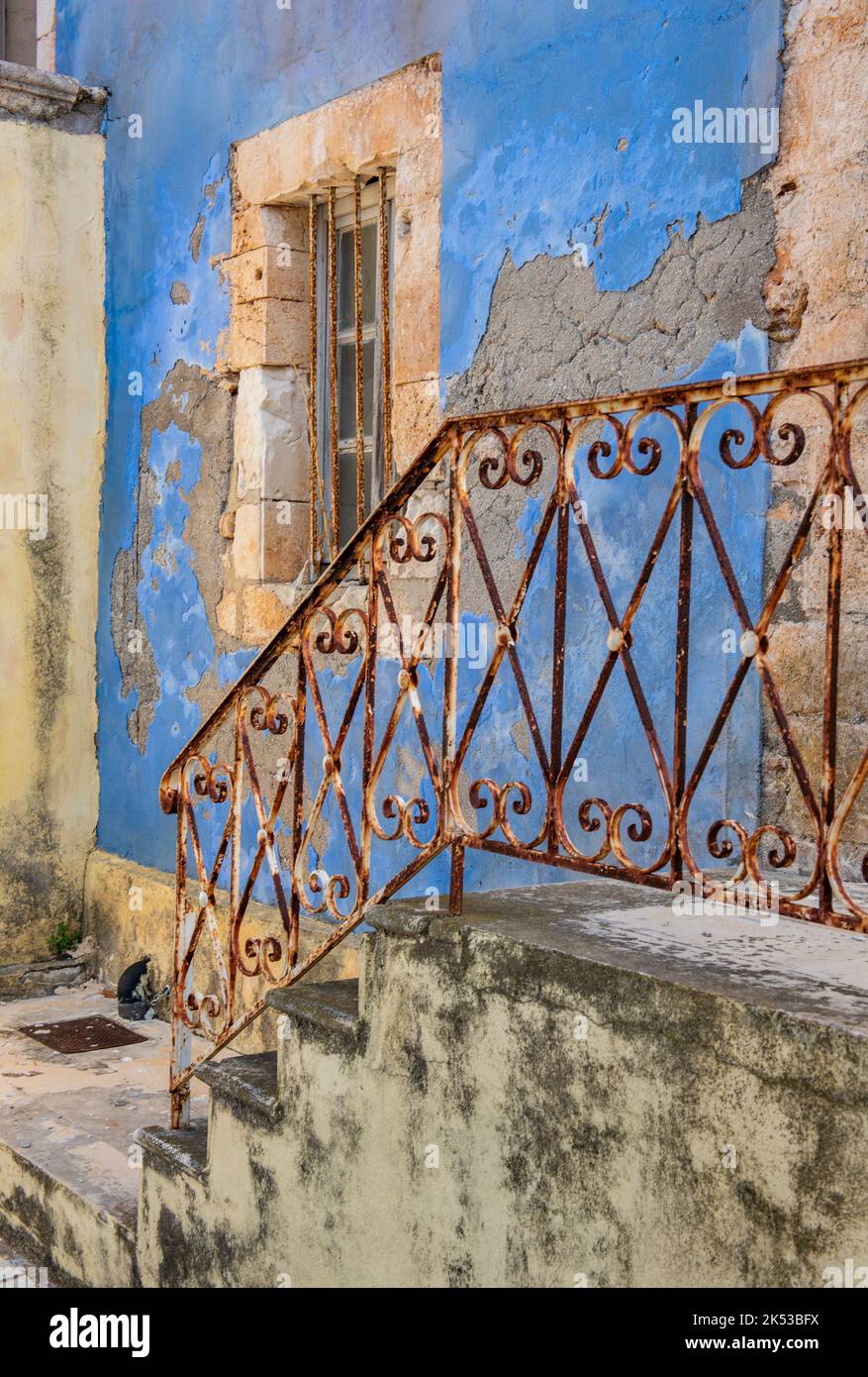 splendido edificio greco in stile elegante e scabro, battuto dal tempo, con pareti dipinte di blu sbiadito e ringhiere arrugginite, dereliche ed edifici intatti. Foto Stock