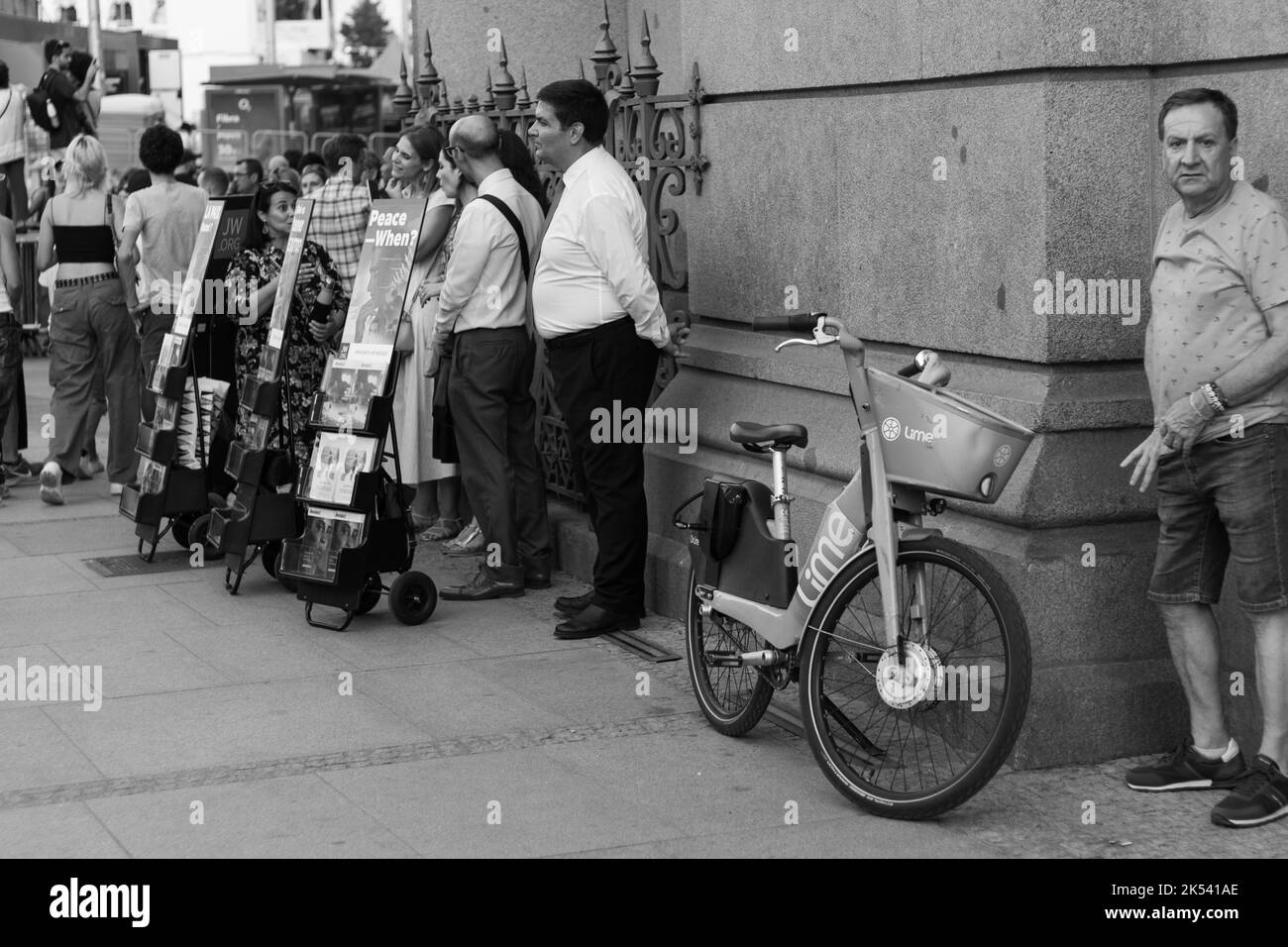 Una scala di grigi di persone e una bicicletta su un marciapiede pavimentato Foto Stock