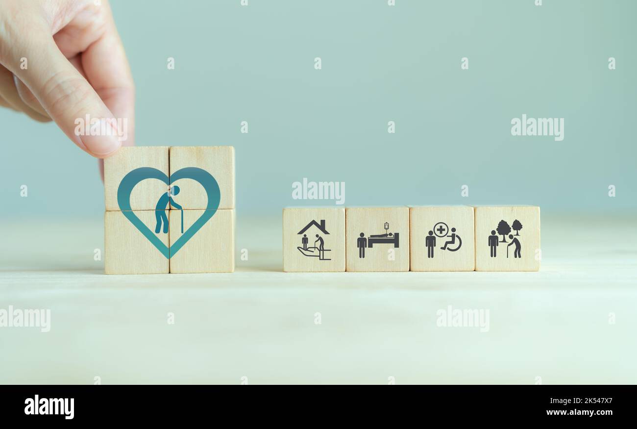 Concetto di assistenza agli anziani. La mano tiene i cubi di legno con le icone relative alla cura anziana, al medico, al servizio di riabilitazione, all'assistenza infermieristica per migliorare la qualità Foto Stock