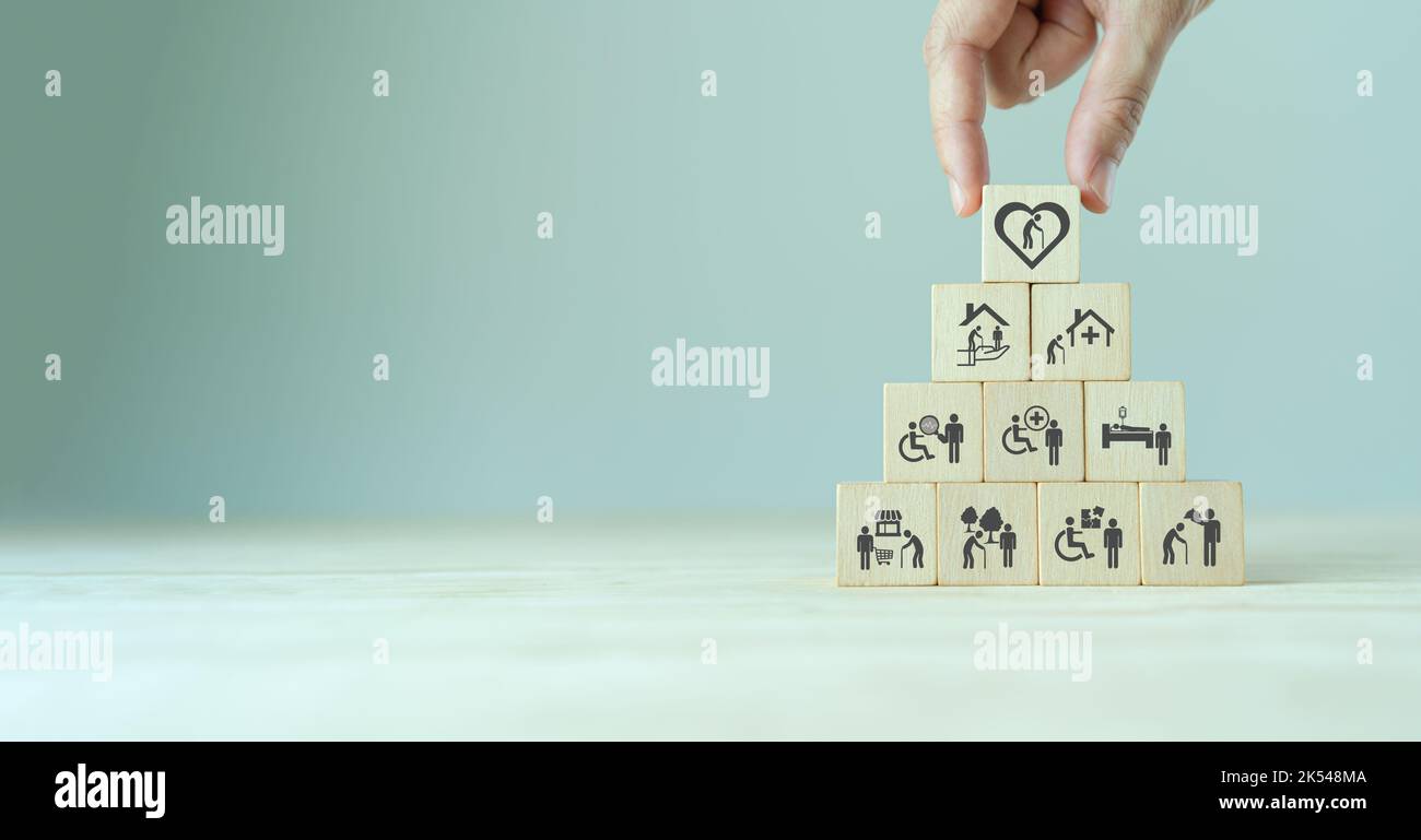 Concetto di assistenza agli anziani. La mano tiene i cubi di legno con le icone relative alla cura anziana, al medico, al servizio di riabilitazione, all'assistenza infermieristica per migliorare la qualità Foto Stock