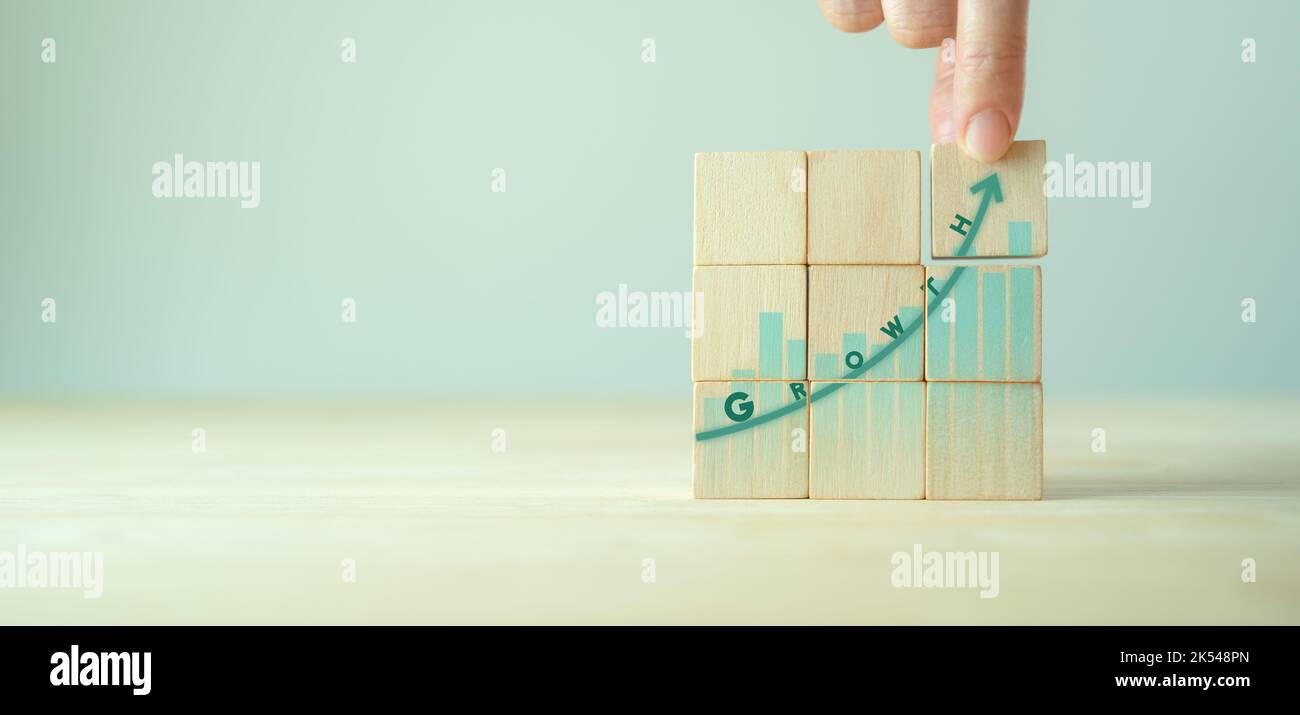 Concetto di crescita e successo. Definizione degli obiettivi e strategie comuni per le aziende. Mano mette i cubi di legno con prestazioni di crescita su sfondo grigio e copia Foto Stock