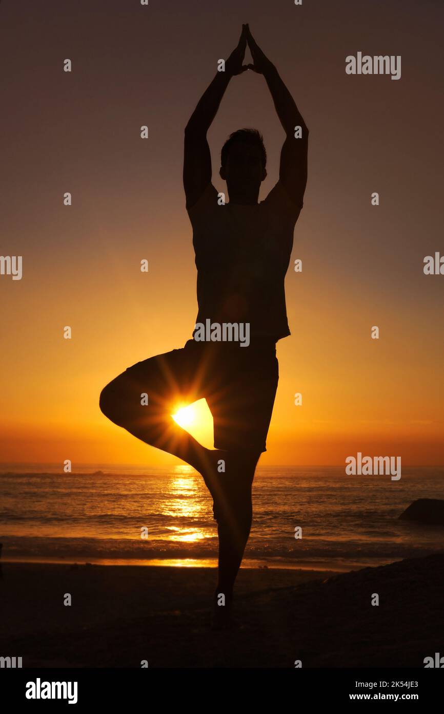 Sentirsi in equilibrio con la natura. Silhouette di un uomo che si bilancia su una gamba contro un tramonto. Foto Stock