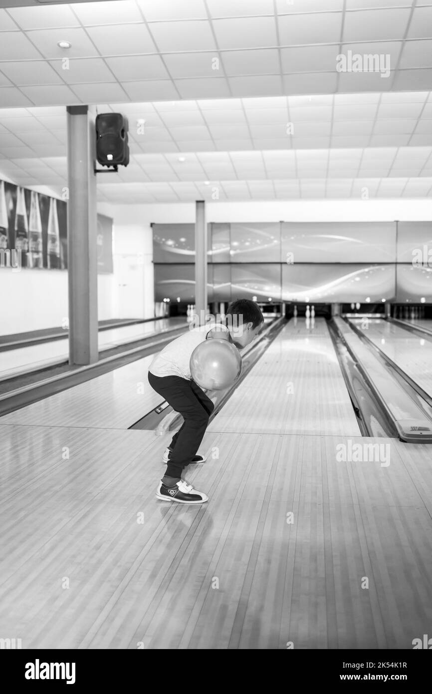 Un bambino lancia una palla in una pista da bowling. Sentieri con palle e spilli per il bowling. Un gioco divertente per l'azienda. Foto Stock