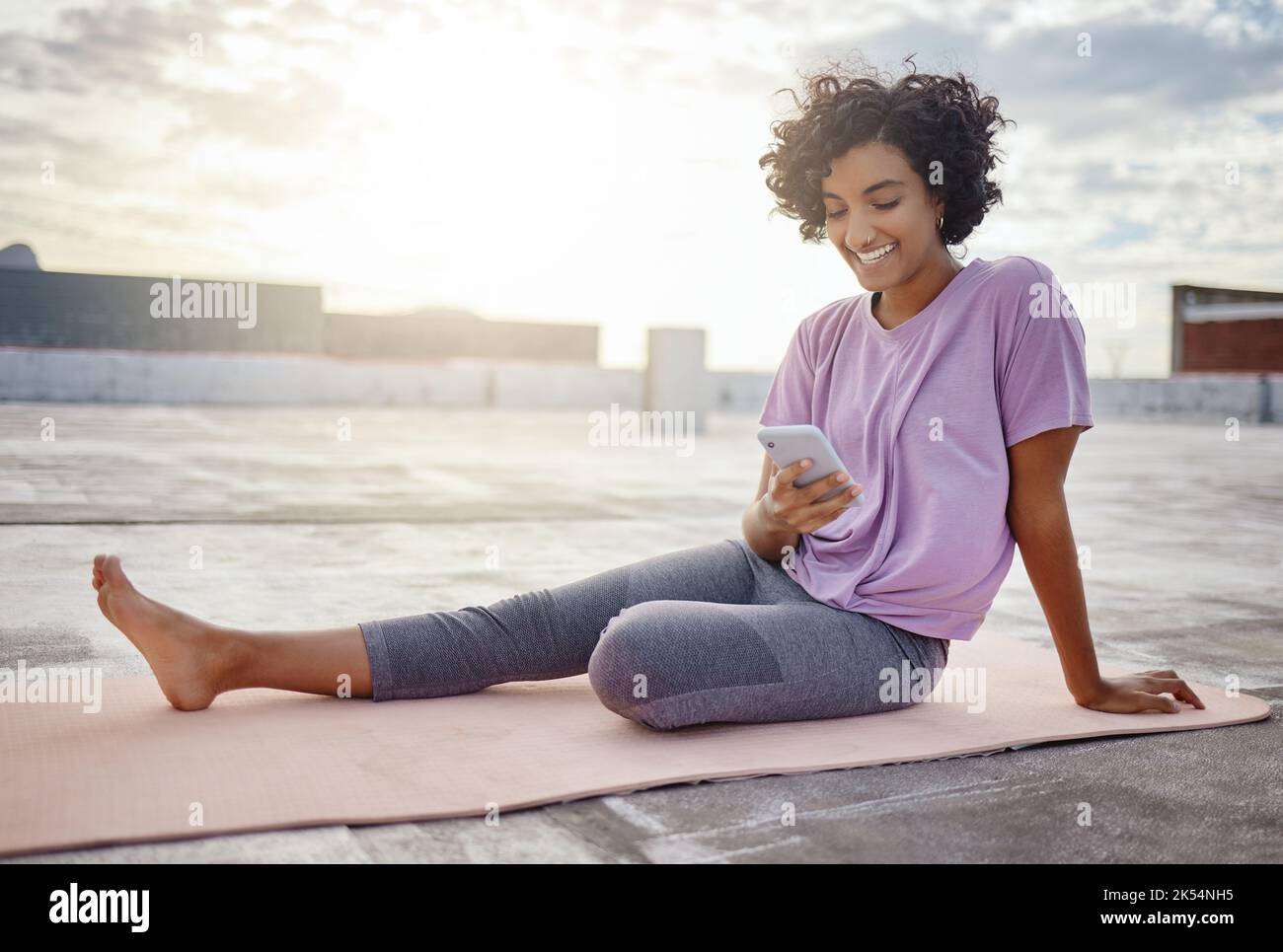 Telefono, social media e yoga con un'atleta sul tetto per il fitness, l'allenamento e l'esercizio fisico in città. Sport, comunicazione e formazione con Foto Stock