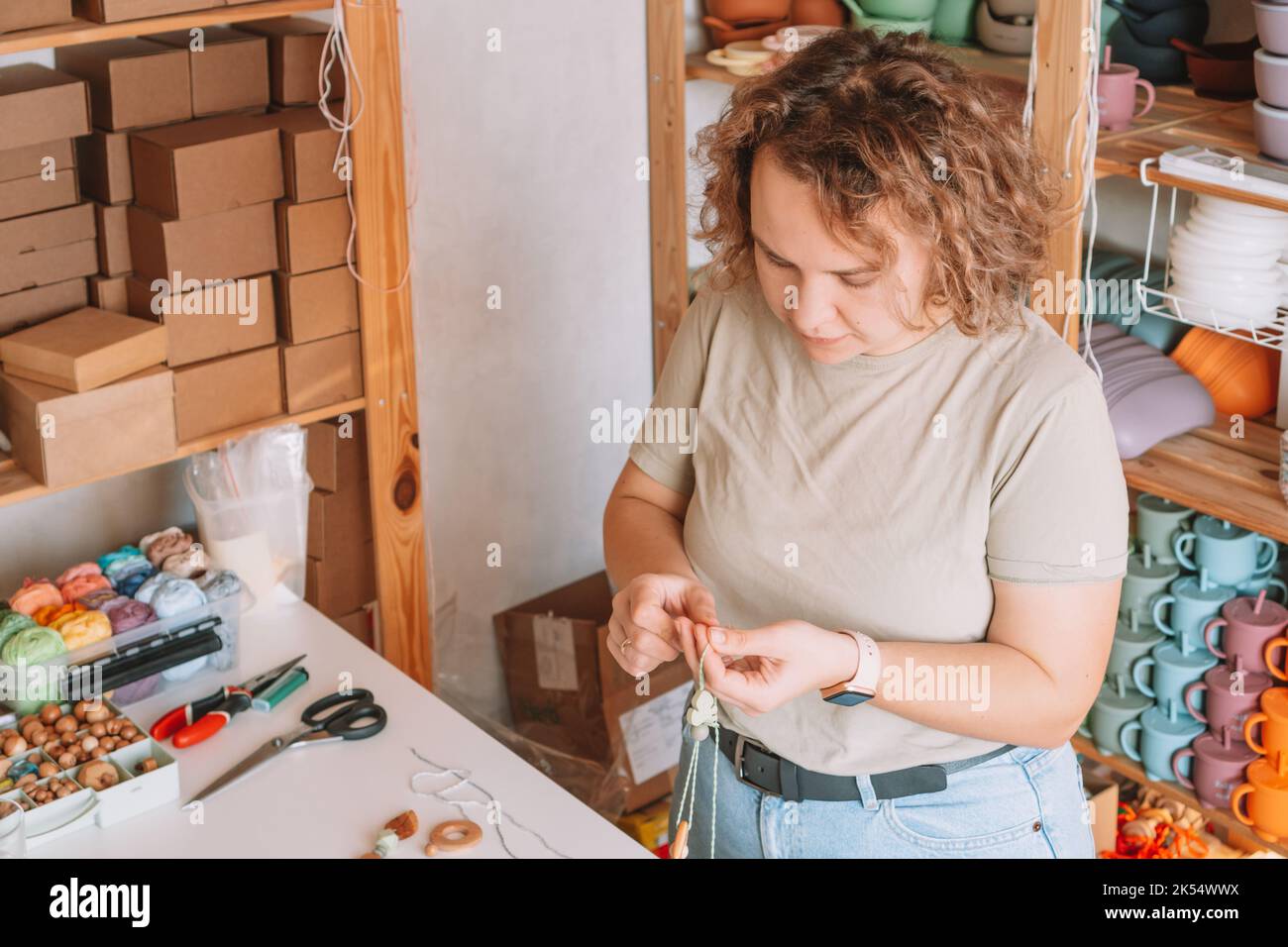 Donna che rende naturale sicuro accessori di legno sulla scrivania, eco stile. Cordoni di articolazione. Teether giocattolo con decorazione trinket sonaglino. Lavorazione artigianale di Foto Stock