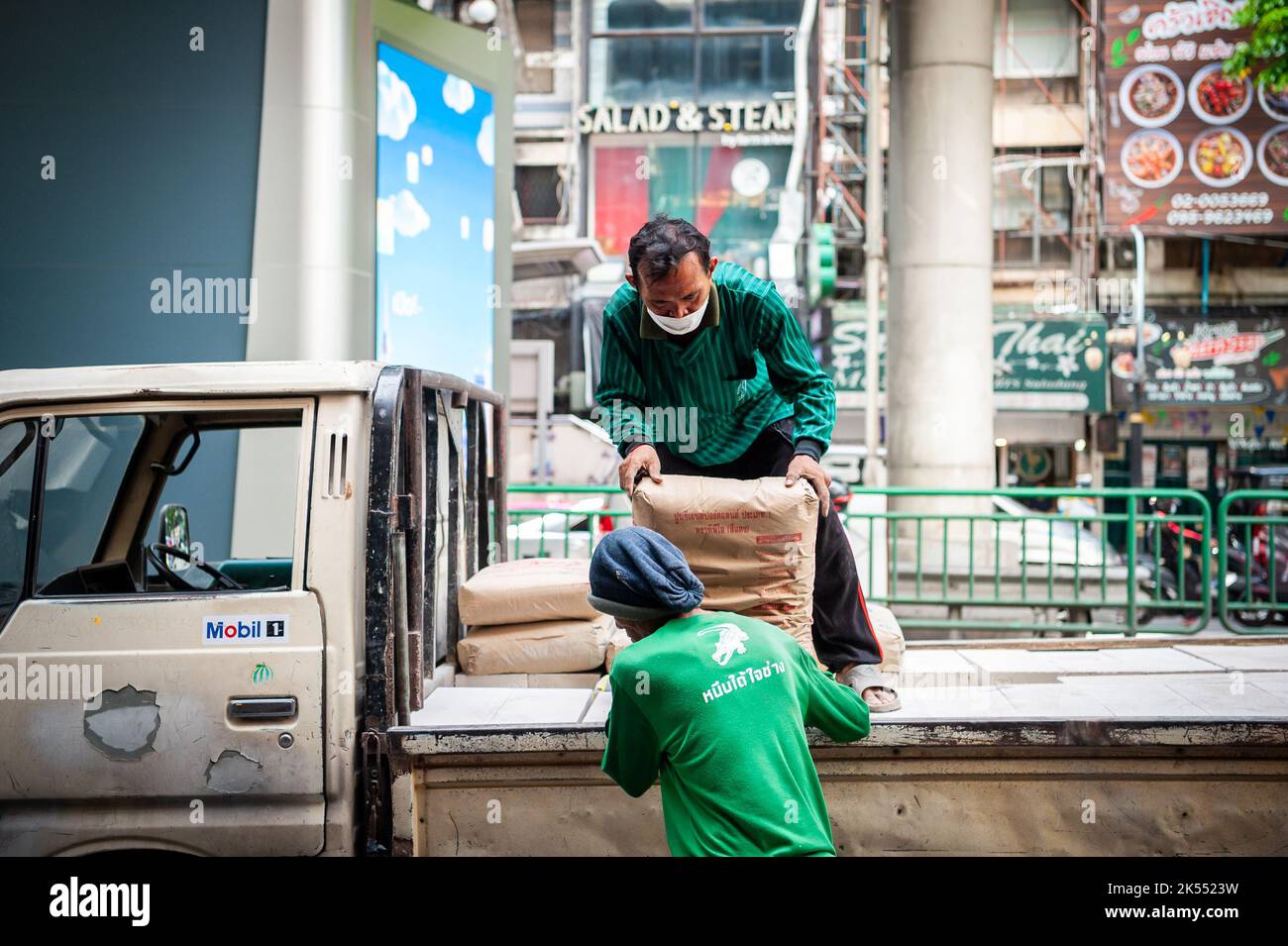 I lavoratori edili thailandesi scaricano cemento o ghiaia dalla parte posteriore di un camion su Silom Rd. Bangkok Thailandia. Foto Stock