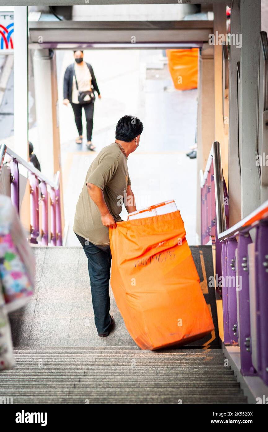 Un uomo thailandese trasporta quello che potrebbe essere un sacchetto per la posta lungo i passi della stazione di Sala Daeng BTS skytrain, Bangkok Thailandia. Foto Stock