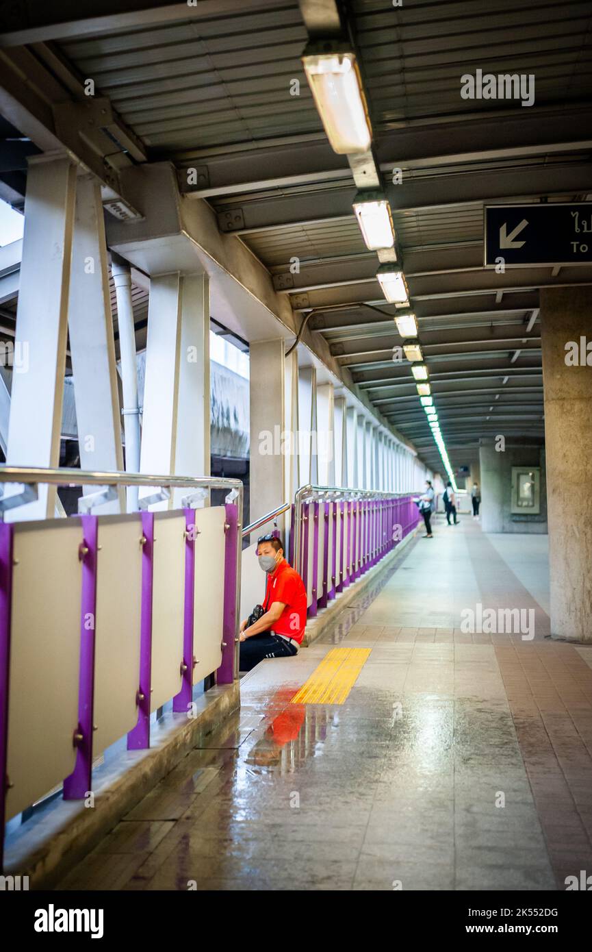 Un uomo thailandese siede sui gradini della Sky Walk sopra le trafficate strade di Bangkok. Foto Stock