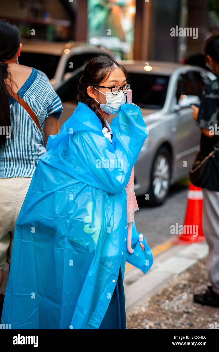 Una giovane ragazza della scuola thailandese aspetta l'autobus che indossa un mac Rain a Sala Daeng, Bangkok, Thailandia. Foto Stock