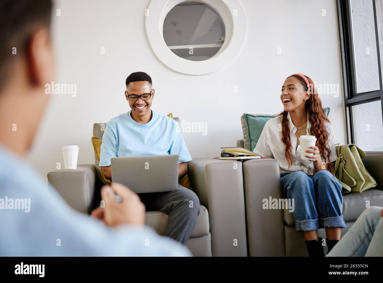 Amici, studenti e diversità nella sala universitaria, ridendo e seduti sul divano con un computer portatile. L'amicizia, l'educazione e gli uomini e le donne felici si rilassano Foto Stock