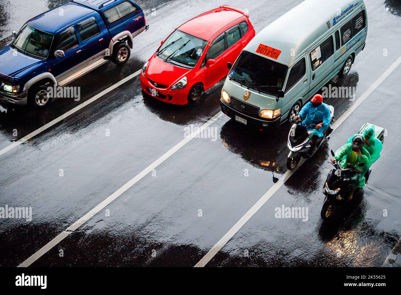 Auto, furgoni, autobus e motociclette passano tutti lungo un incrocio affollato in una giornata buia e piovosa durante l'ora di punta a Bangkok, Thailandia. Foto Stock