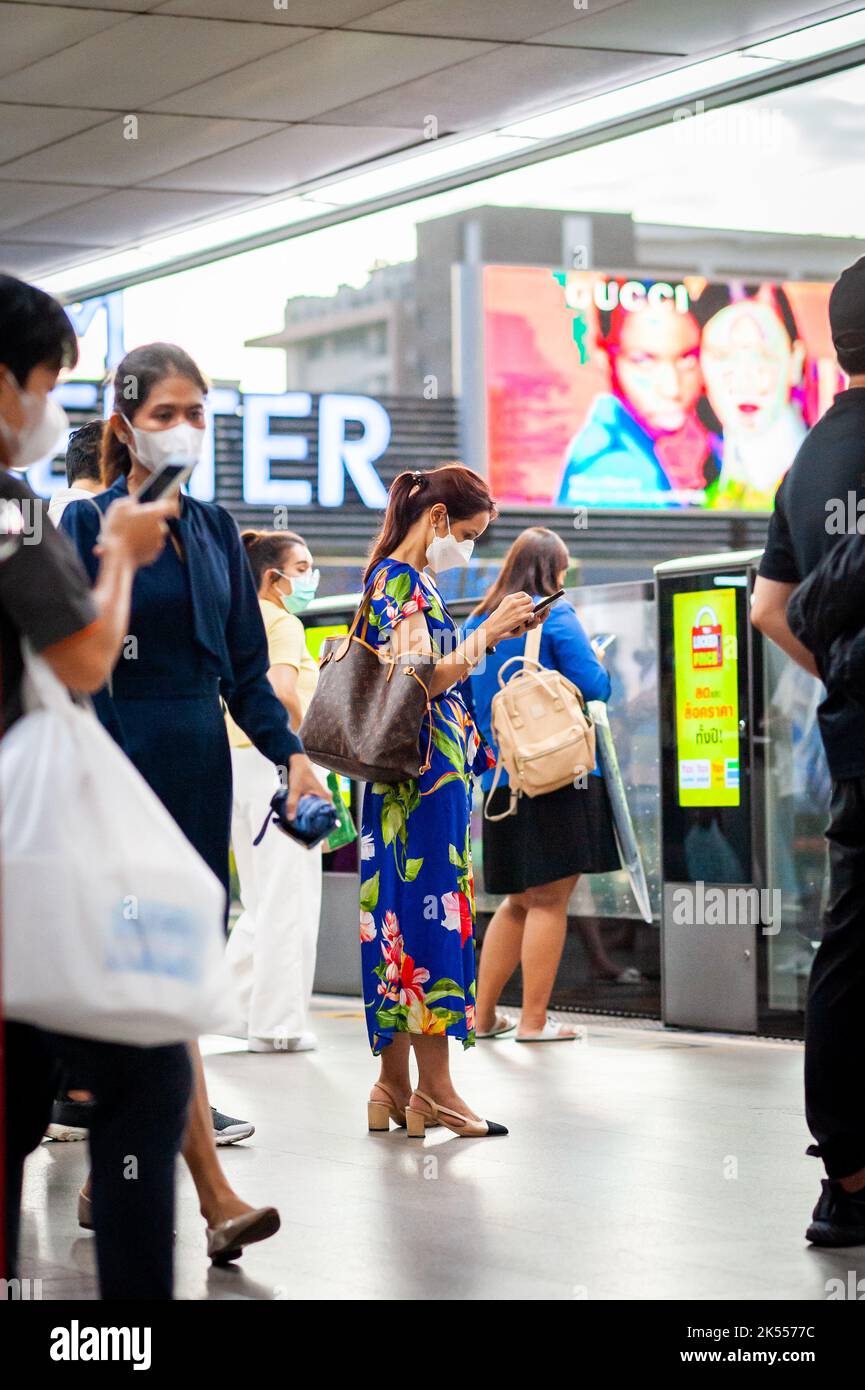 Un'elegante signora tailandese utilizza il suo telefono alla stazione del treno sopraelevato Siam BTS mentre attende il suo treno. Foto Stock