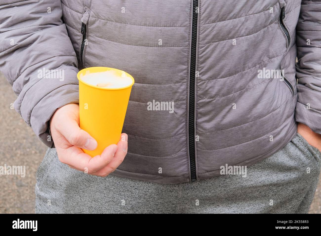Mani umane che tengono una tazza da caffè di carta con cappuccino, social media. Tazza di carta in mano all'uomo in giacca grigia. Foto Stock