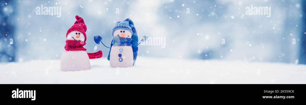 Piccoli pupazzi di neve a maglia sulla neve bianca su sfondo blu. Foto Stock