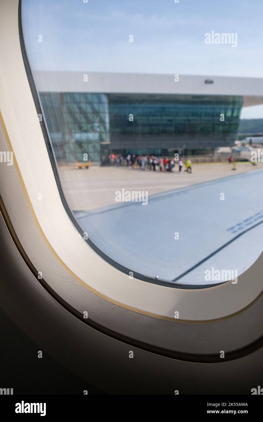 Vista da una finestra di un aereo in un aeroporto, con una coda di persone in distanza lasciando le partenze per il loro aereo. Foto Stock