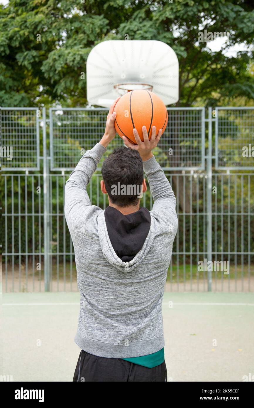 Vista posteriore di un uomo sportivo che lancia una palla al basket in un campo da basket all'aperto Foto Stock