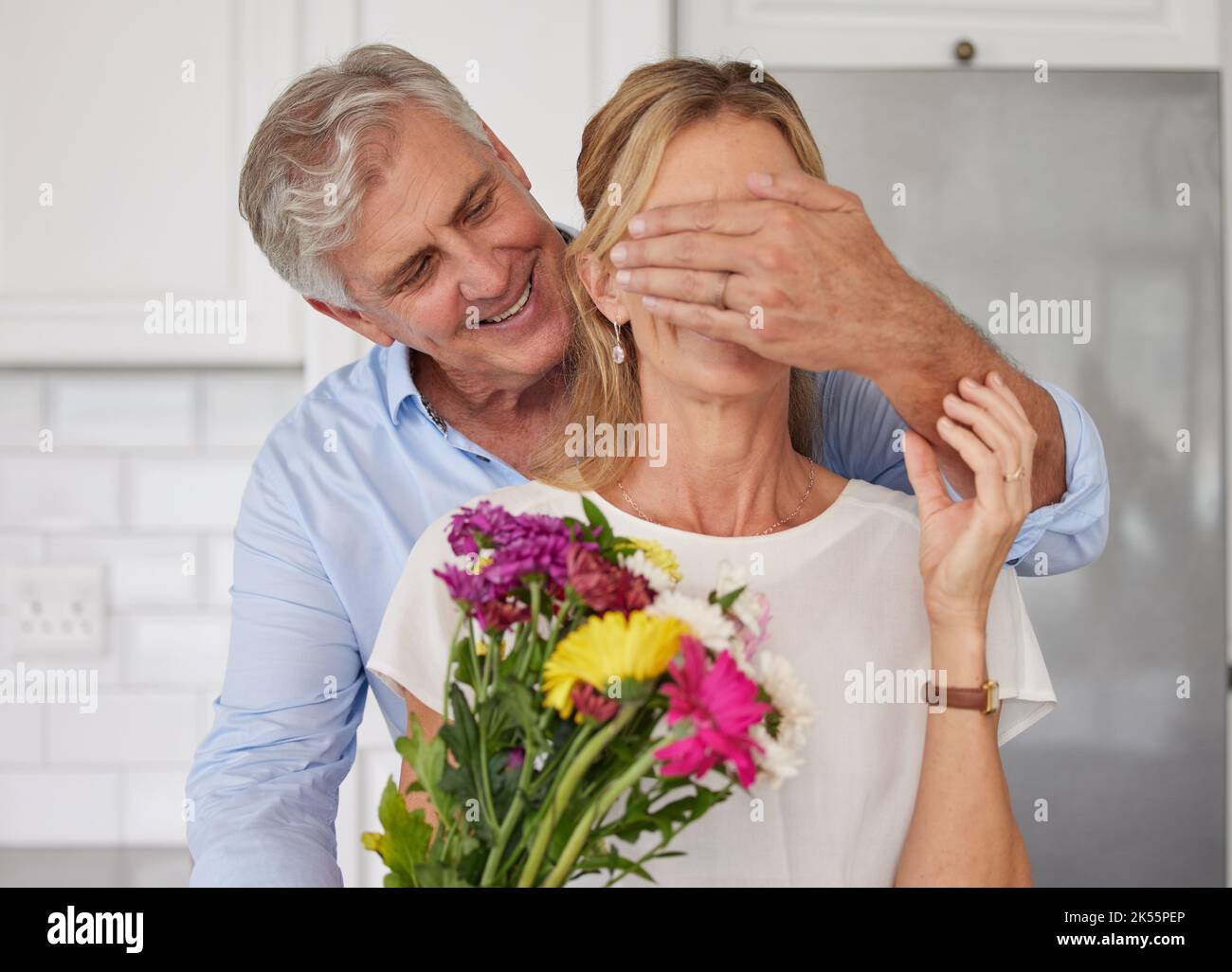 Coppia anziana che copre gli occhi per i fiori sorpresa, l'amore anniversario e giorno di San Valentino in Nuova Zelanda casa. Uomo felice che dà bouquet alla donna per Foto Stock